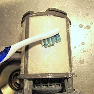 brushing limescale and detergent residue off a dishwasher upper filter using CLR and a toothbrush