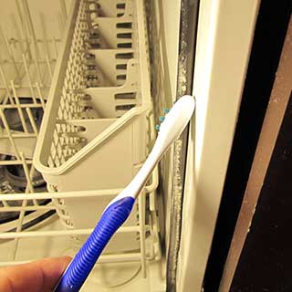 brushing buildup off a dishwasher door seal using a toothbrush and CLR